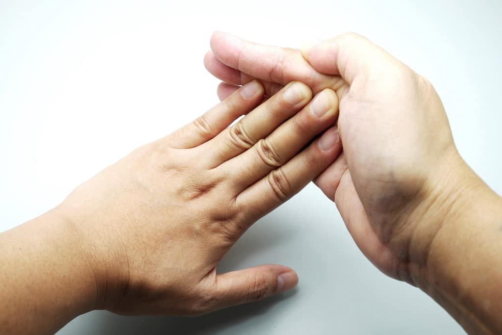 Woman flexing/stretching fingers against hand on gray background.