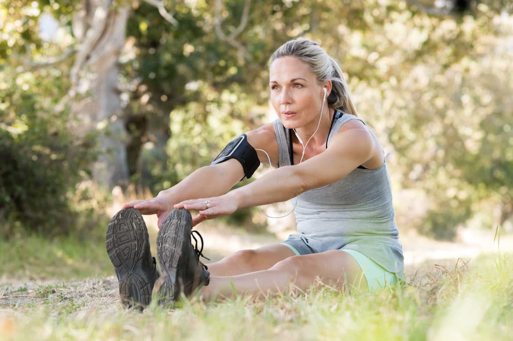 Senior woman exercising in park while listening to music. Senior woman doing her stretches outdoor.