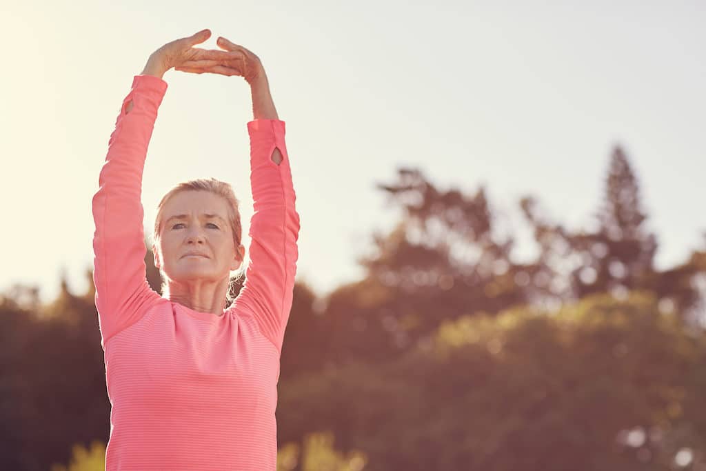 Sporty senior woman doing exercise warm-up stretches outdoors