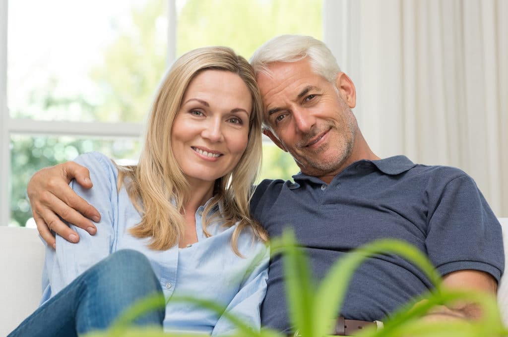 Romantic senior couple sitting on a sofa and looking at camera. Portrait of a mature couple enjoying their retirement. Happy smiling senior couple embracing together at home.