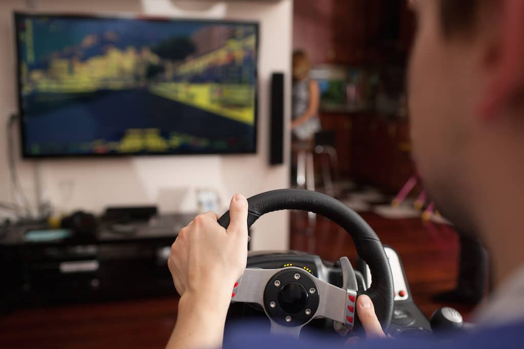 Back close-up shot of a man playing car racing video game using steering wheel
