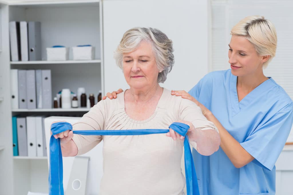 Nurse helping senior patient in exercising with resistance band in clinic