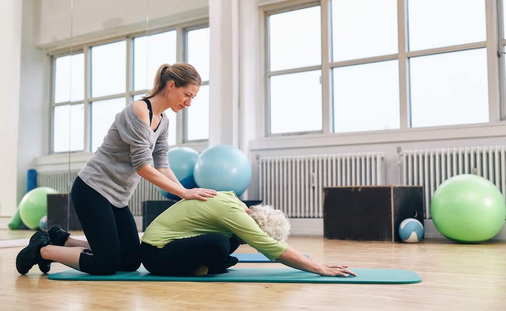 Physical Trainer Helping Elder Woman Doing Yoga