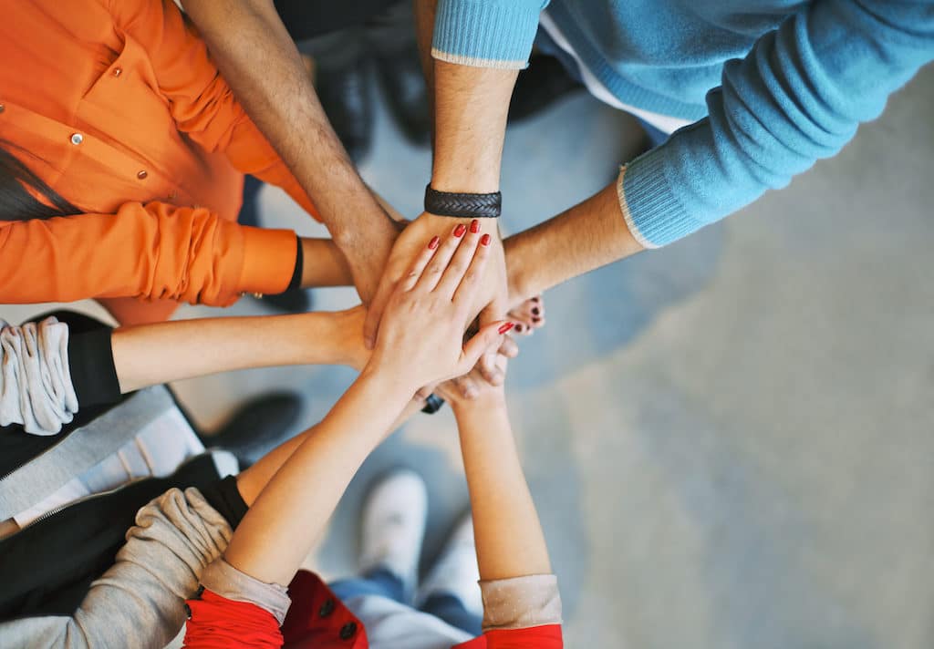 Top view image of group of young people putting their hands together. Friends with stack of hands showing unity.