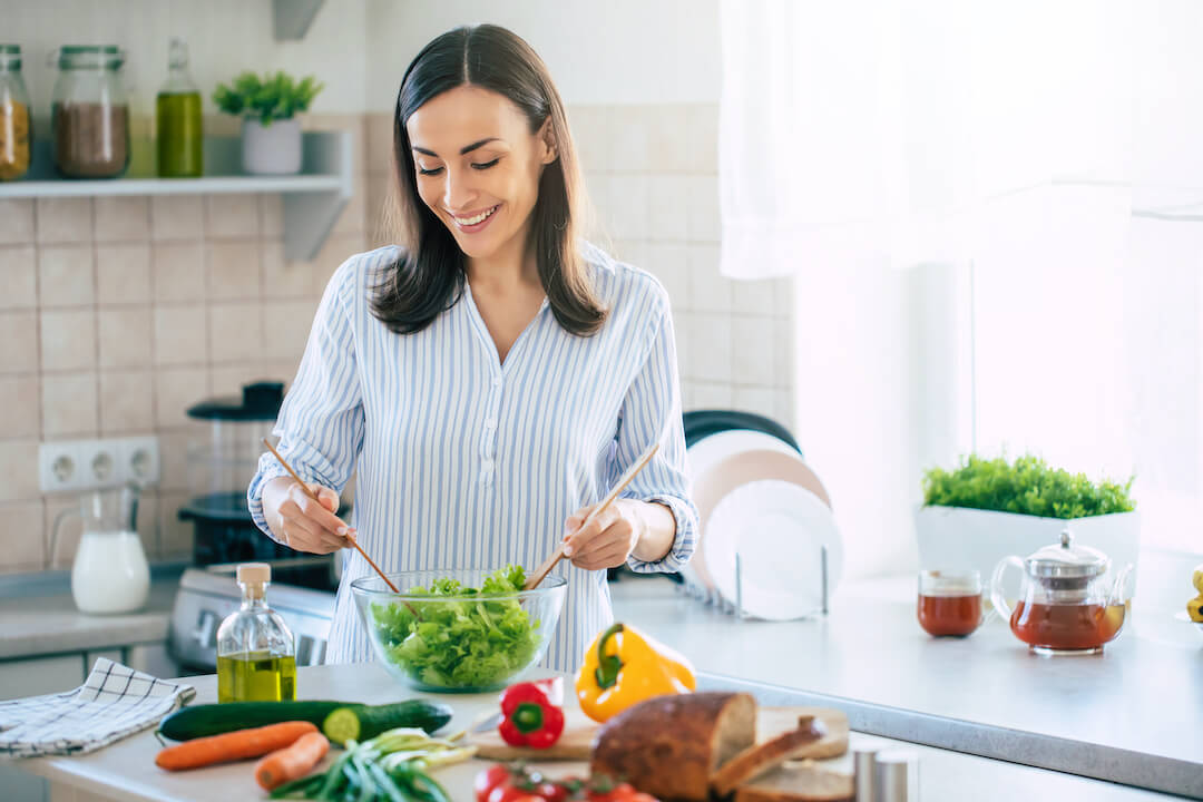 Woman standing in kitchen making a salad.