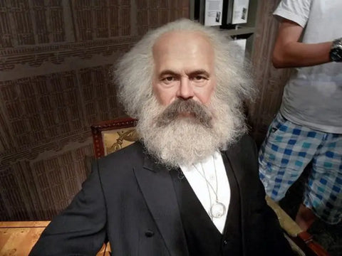 Wax figure of Karl Marx, the philosopher and political theorist, with a full gray beard and suit, displayed in a museum setting.