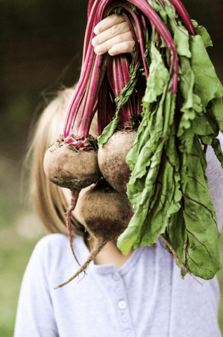 Young girl holding up a handful of beets.