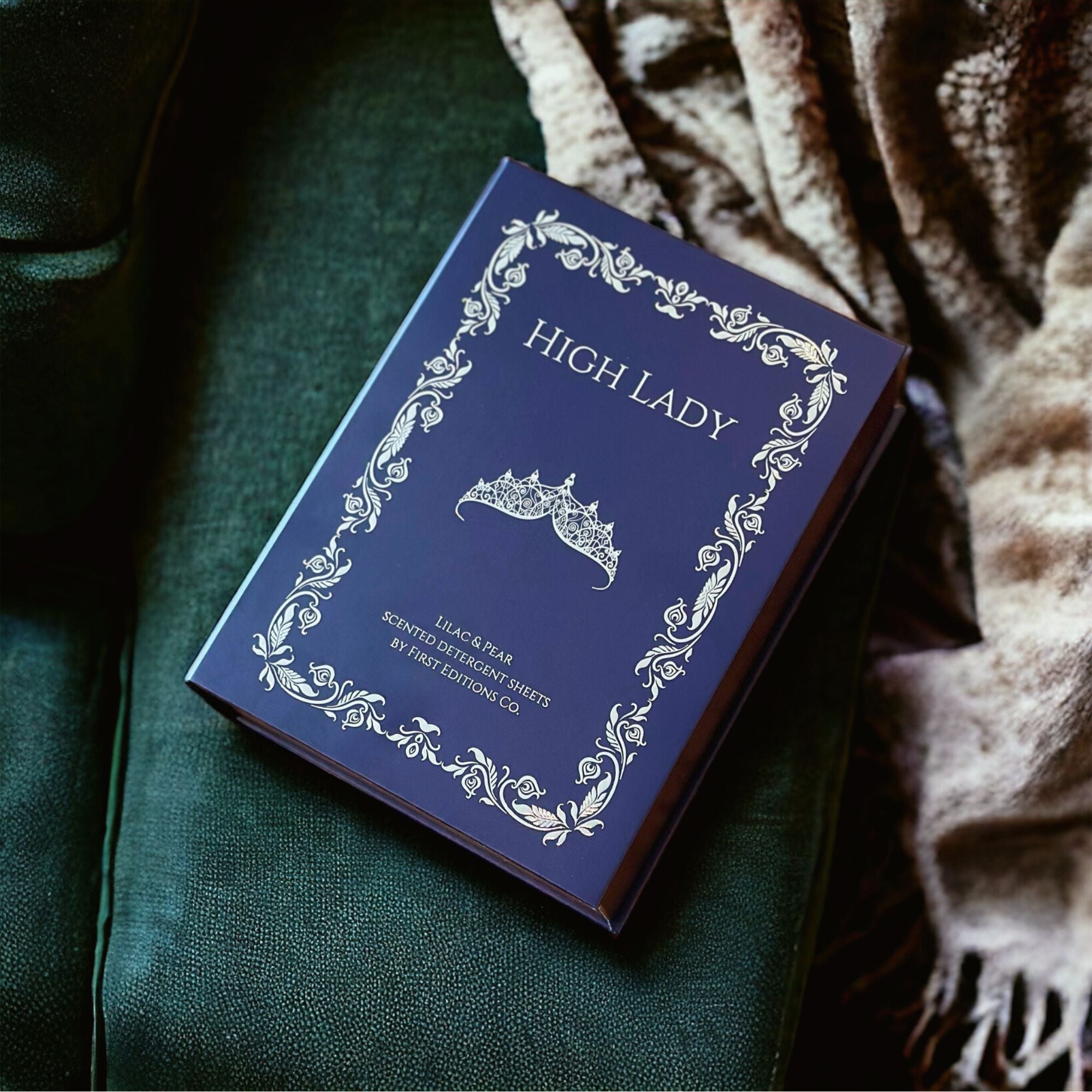 Navy blue book titled 'HIGH LADY' on a green cushion with a blanket.