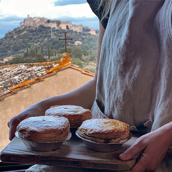 woman holding pies with a view of hilltop village in background