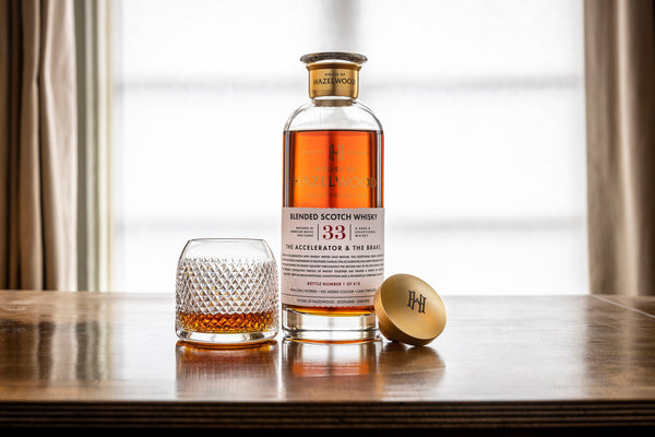 A bottle of The Accelerator & The Brake whisky sits on a table alongside a pour of the whisky in a crystal glass.