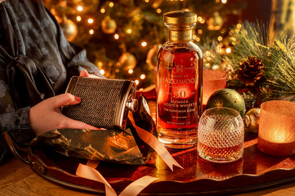 A bottle of The Huntsman Blend and a hipflask whisky gift being unwrapped on a table surrounded by Christmas decorations