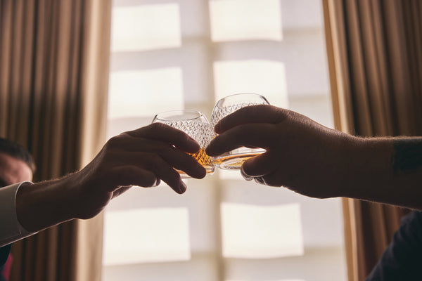 Two hands clink together whisky tumblers in a motion of celebration