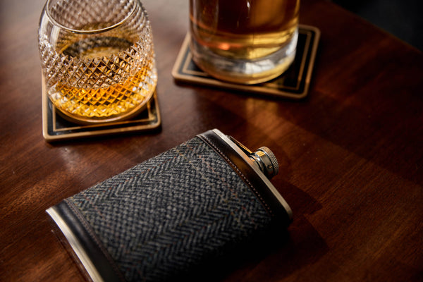 A Huntsman Hipflask lies on a walnut table next to a House of Hazelwood tumbler of whisky.