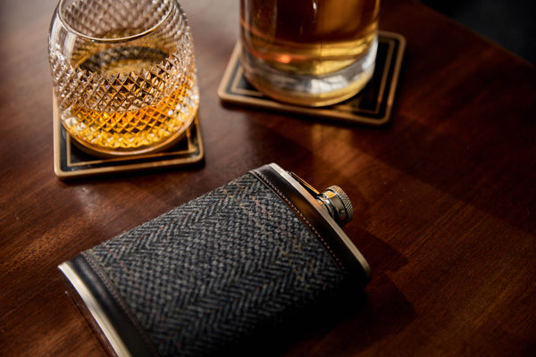A picture of a Huntsman tweed bound hipflask and a tumbler of whisky.