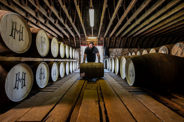 House of Hazelwood whisky casks in dunnage warehouse and a cask being rolled by a warehouseman