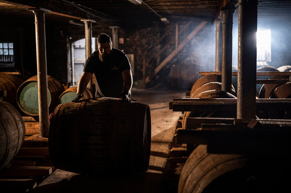 George rolls a cask down a path between two rows of casks