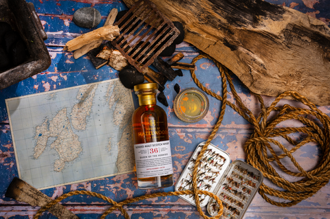 A bottle of Queen of the Hebrides Scotch Whisky lies on a table surrounded by fishing paraphernalia.