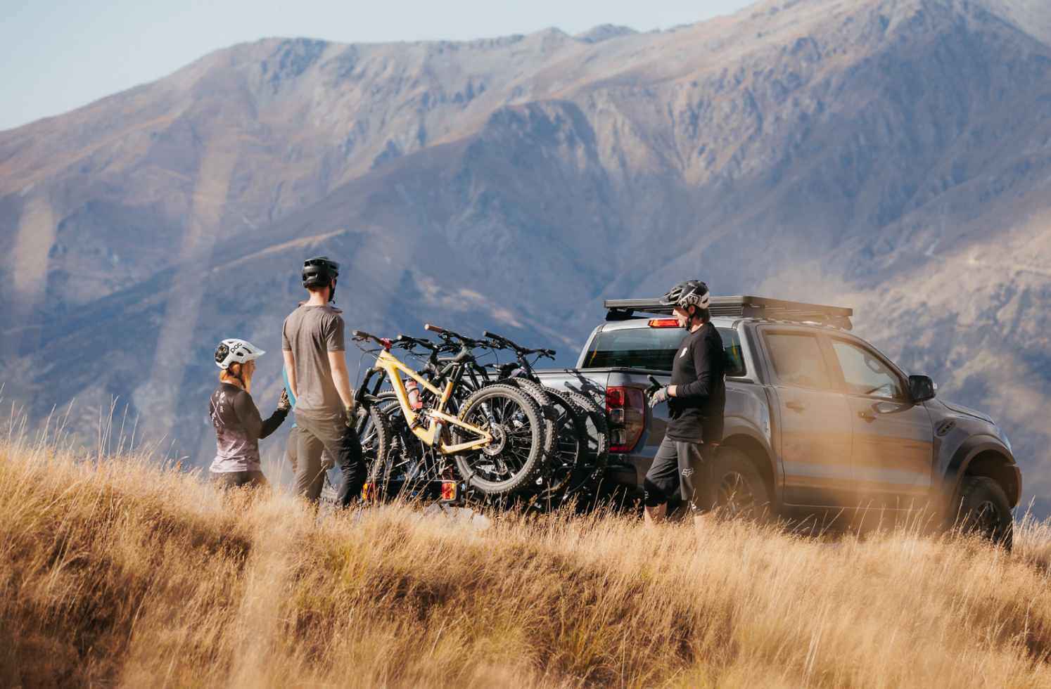 Mountain bike riders are standing around a ute with a platform bike rack on the towbar.