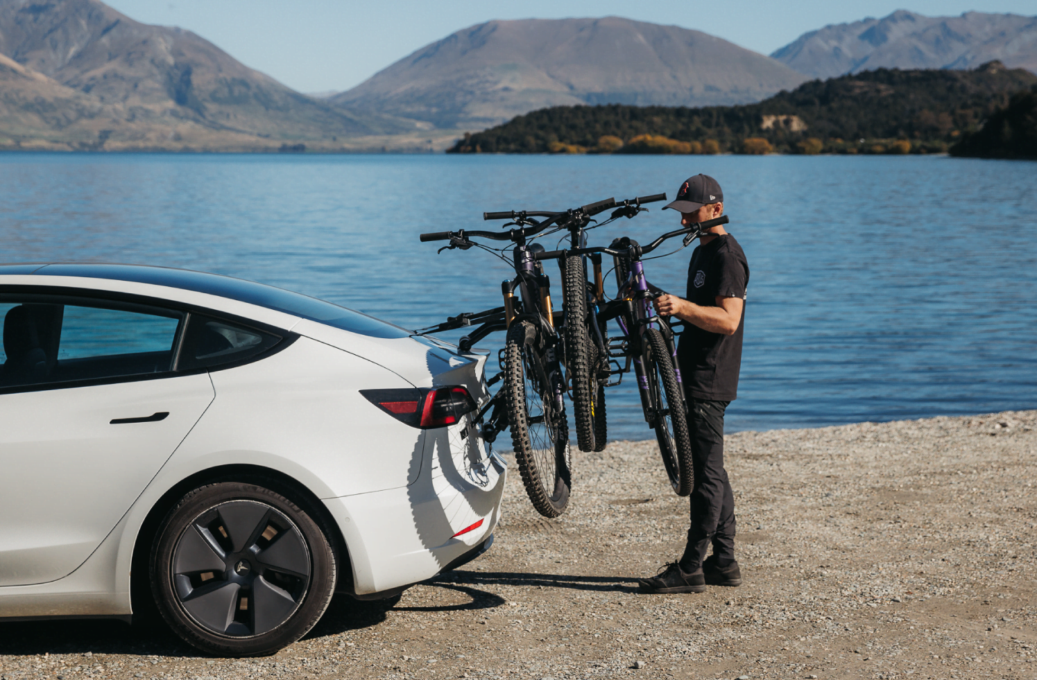 An electric vehicle is by a lake with a boot mounted bicycle carrier strapped to the trunk of the car.