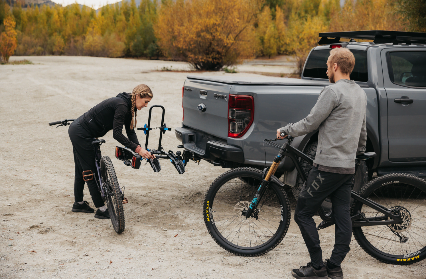 A woman is leaning over an Enduro 2 bike rack that is mounted to the towball of a ute.