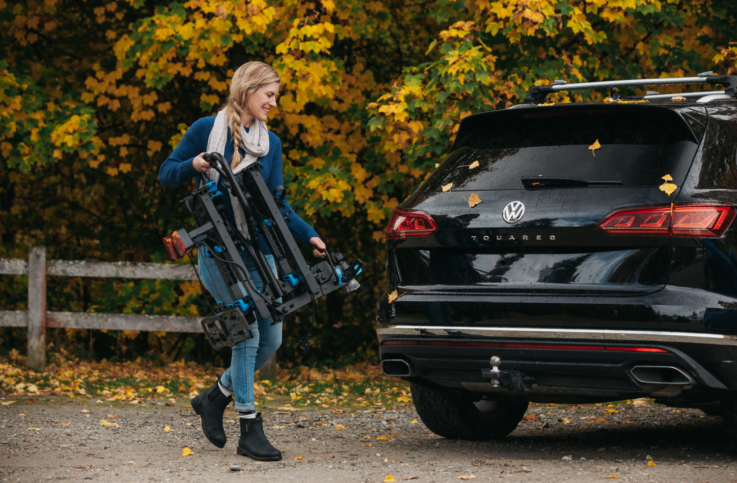 A woman carries the Ezigrip E-Rack 2 bike rack to the back of her SUV. The rack is folded and compact, sitting close to her body.