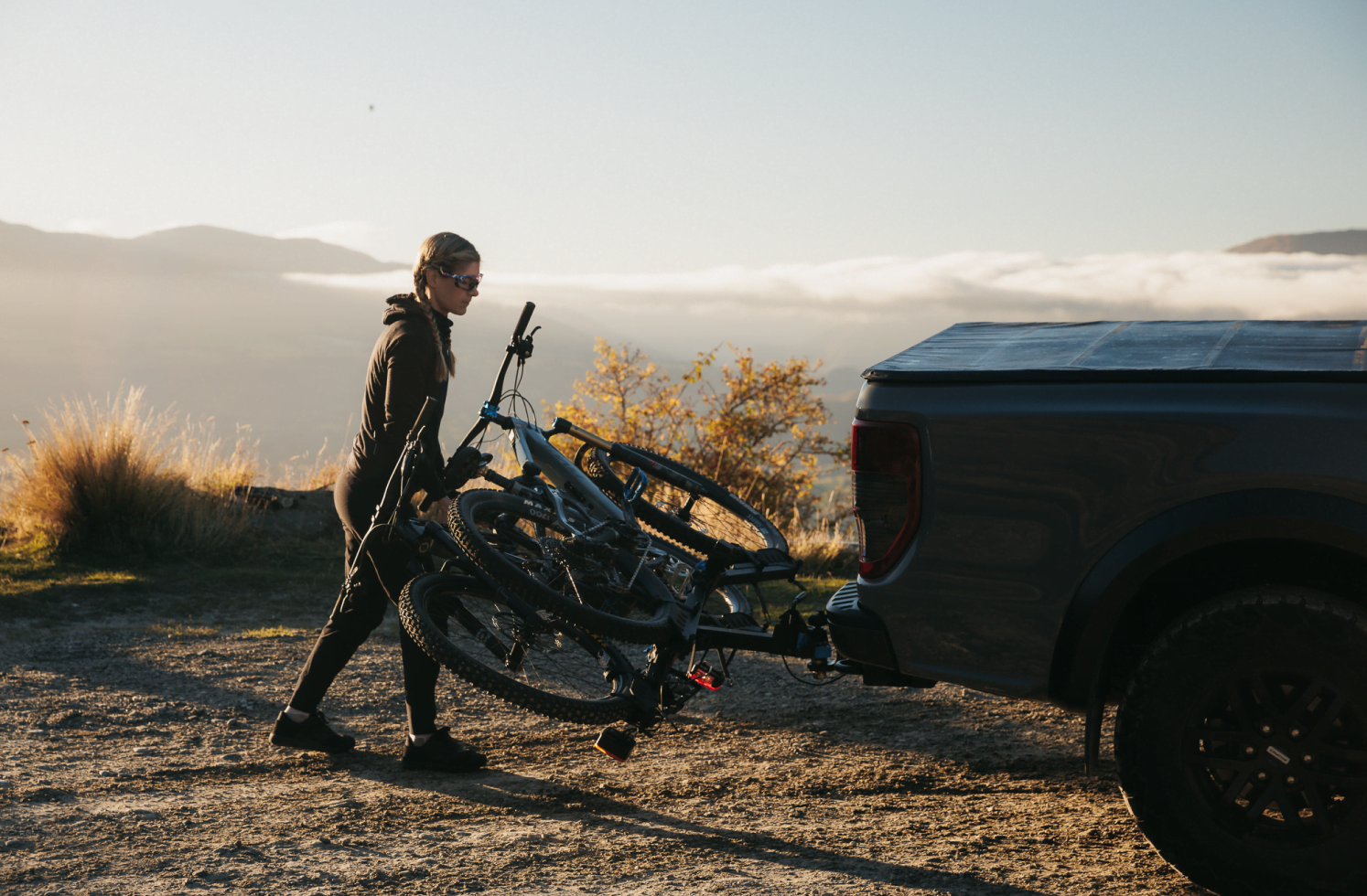 A woman tilts the Ezigrip E-Rack 2 on the back of her ute. The bike rack has two emtbs strapped in and she tilts them along with the rack.