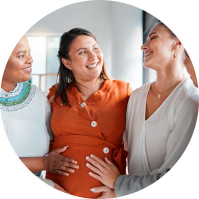 A pregnant women smiles between two friends who place their hands on her belly.