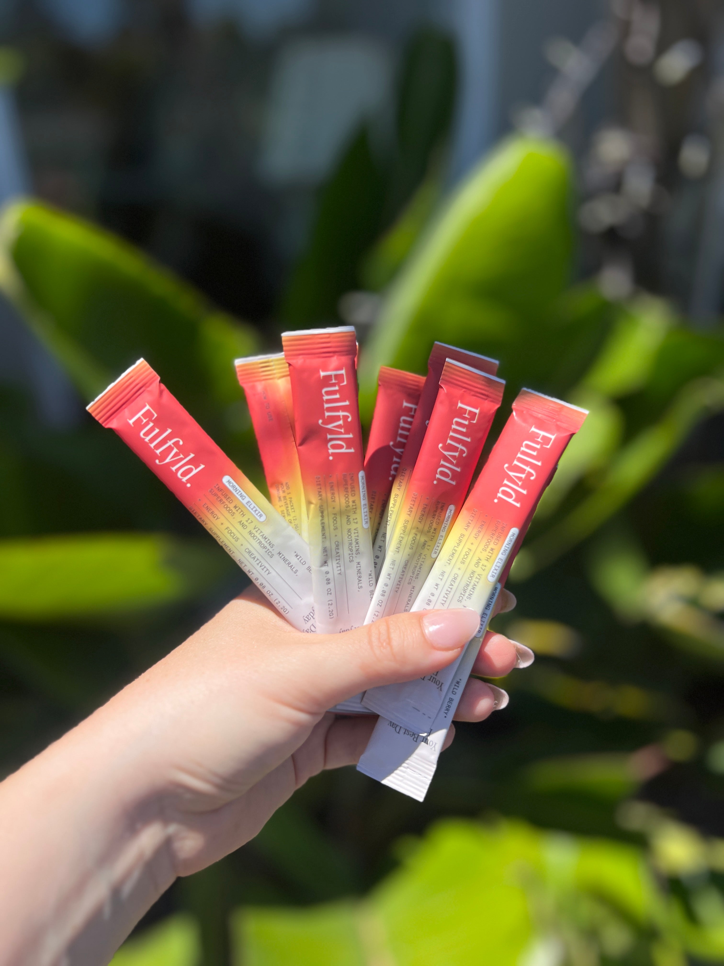 A hand holding several Fulvlyd supplement packets with a leafy green background.