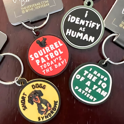 4 of our 17 styles of rubber dog tags. Dog Collar Bling in the photo includes Squirrel patrol, Short Dogg Syndrome with Dachsund, I have the IQ of a Yam. Be patient. I Identify as human.