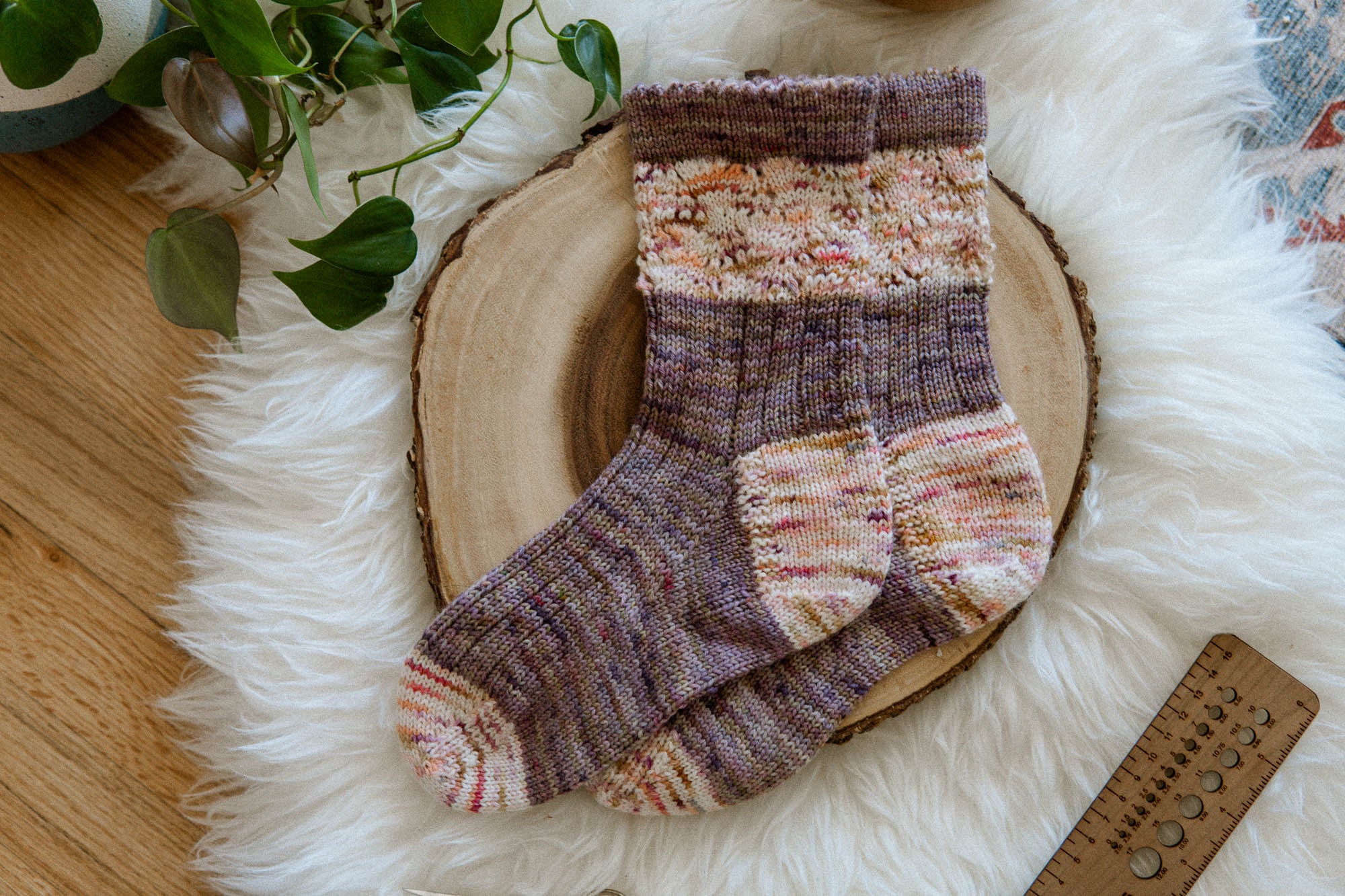 Pair of handknit socks knit from the Wisteria Bloom Socks pattern, knit in purple and cream with speckles. They feature lace and ribbing elements, and a heel flap and gusset construction. Pattern by Aimee Sher Makes.