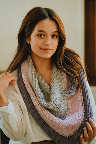 A brown skinned woman smiles slightly while wearing a garter textured shawl in pink, charcoal, and gray.