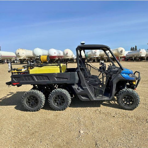 A modern black utility vehicle equipped with agricultural tools, including a yellow tank and spraying equipment, parked in a yard with storage tanks in the background under a clear blue sky.