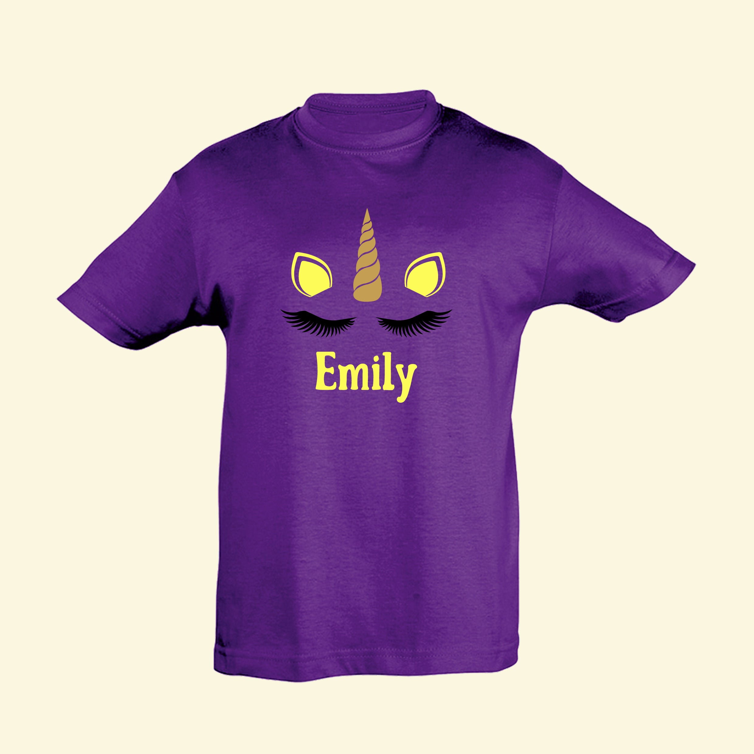 Kids purple t shirt with Emily printed below black eyelashes, golden horn in the middle of two lemon yellow ears matching the text.