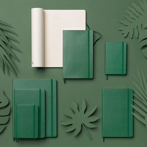 A set of green Moleskine notebooks laid on a green background with leafy props made of a solid material