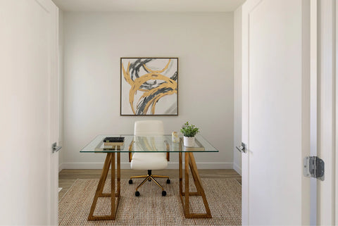 Home office with glass desk, white chair, and gold painting hanged above