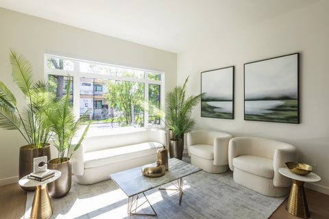 Living room with white chairs, wall art, and plants near open window