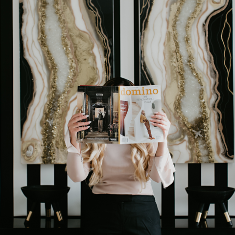 Woman holding magazine in front of face in front of decorated wall