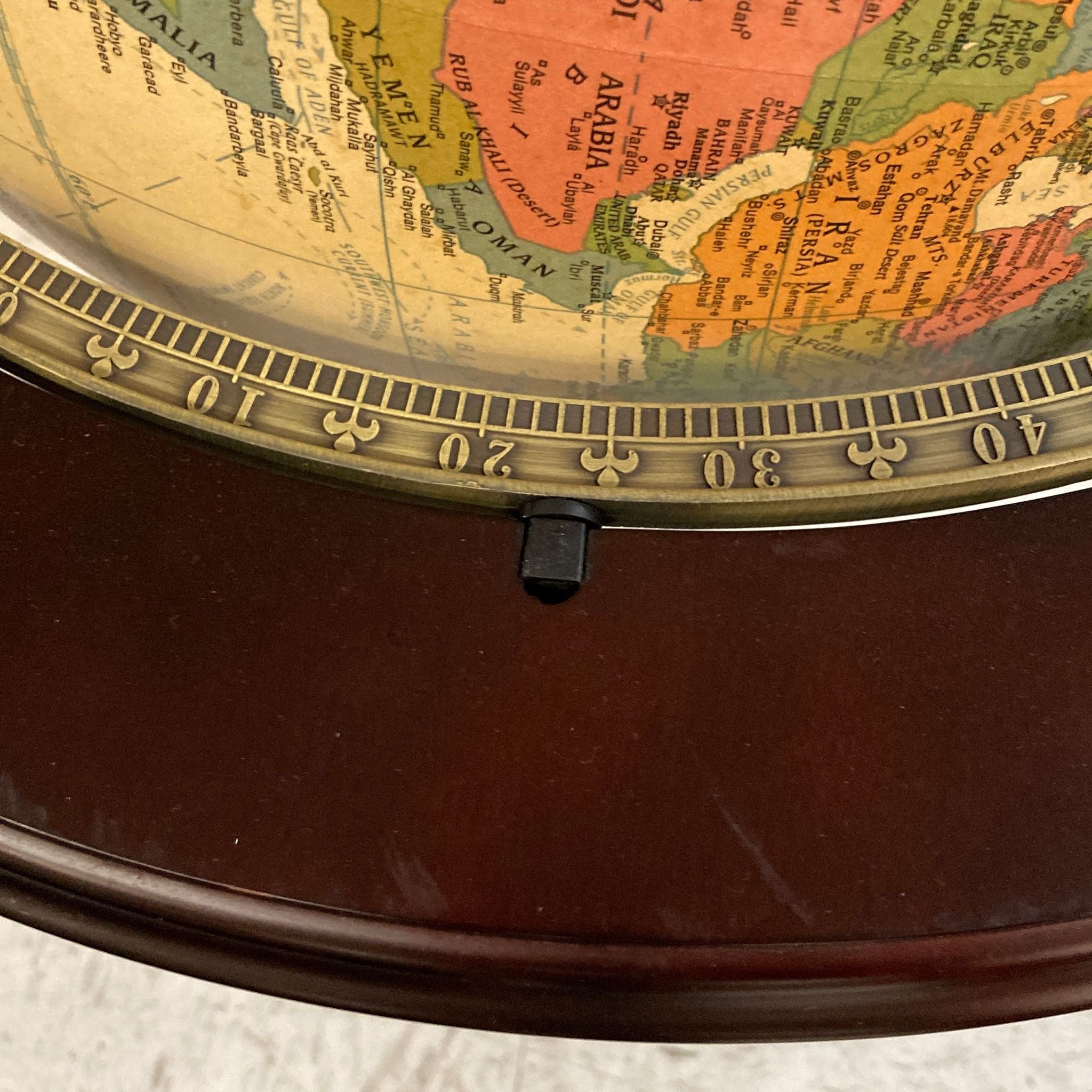 Close-up of antique illuminated globe on cherry wood stand showing detailed map and graduated meridian scale.
