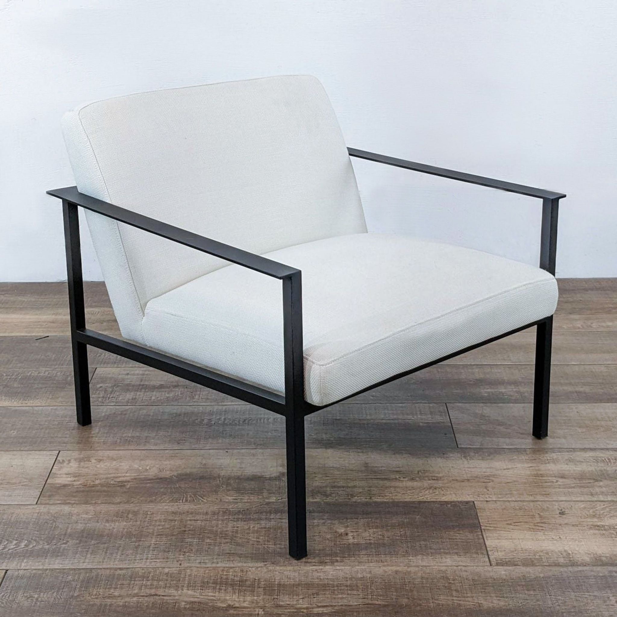 CB2 Cue chair with a sleek matte black frame and textured white fabric on a wooden floor, representing modern lounge style.