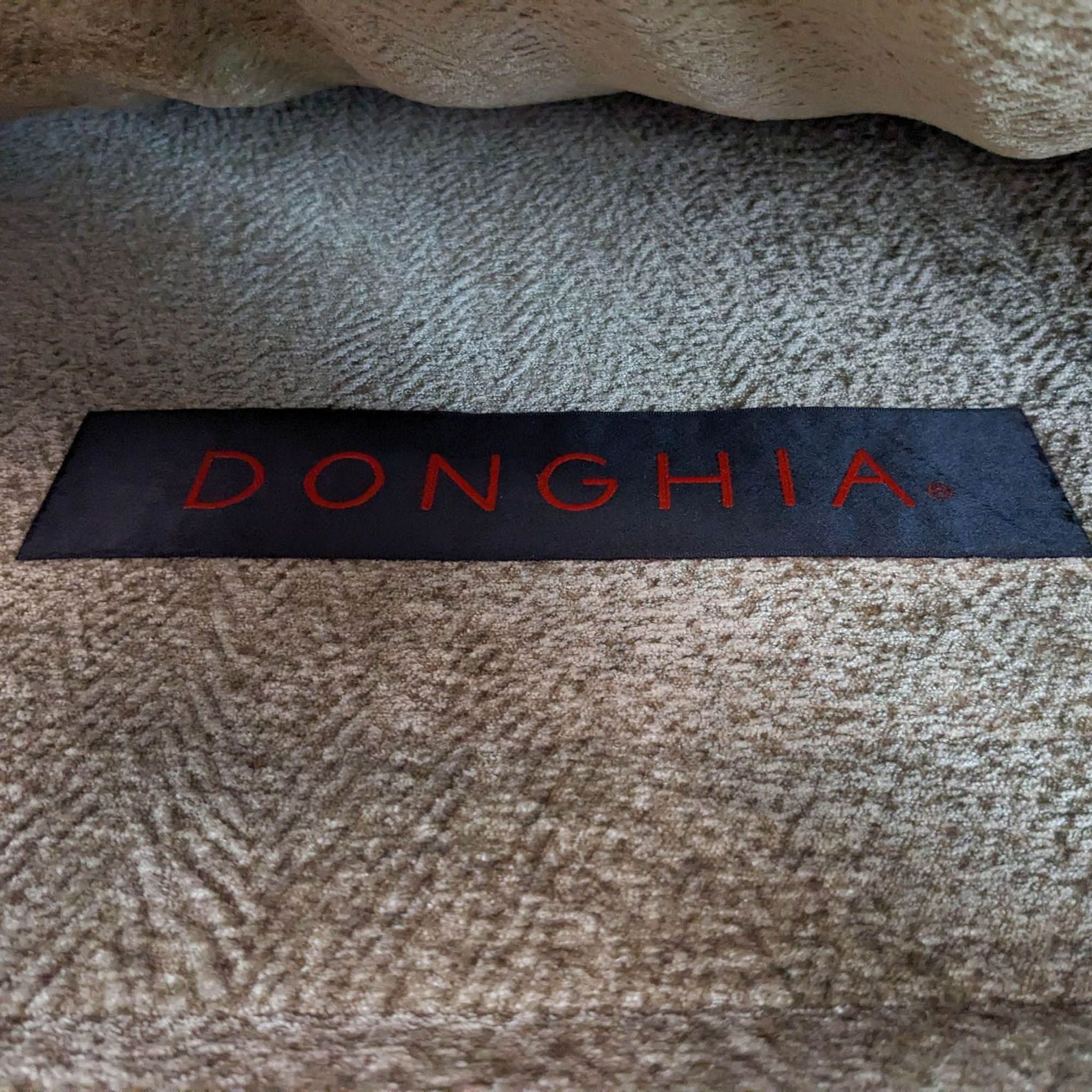 Close-up of Donghia brand label on beige fabric upholstery of a high-end daybed.