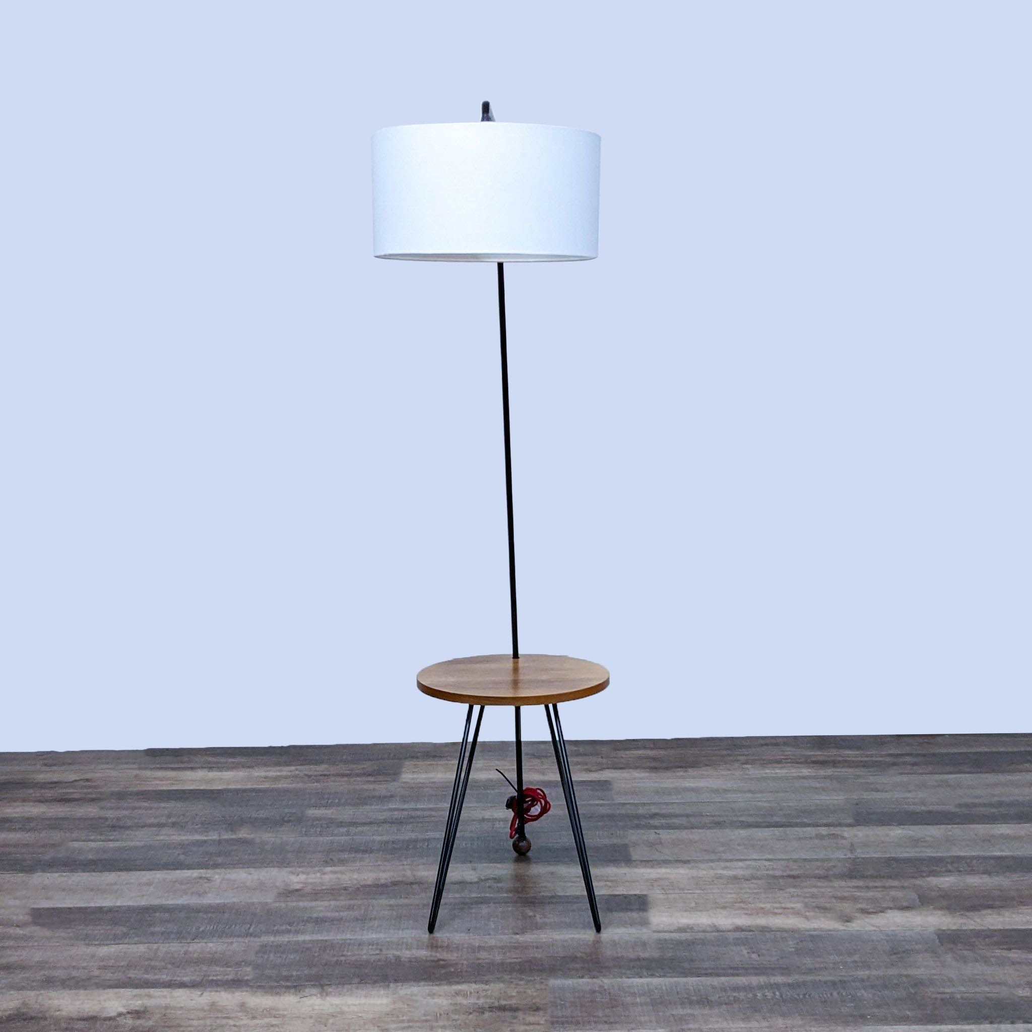 Minimalistic Reperch floor lamp featuring a white drum shade, sleek black stand, wooden shelf, and red-wheeled base.