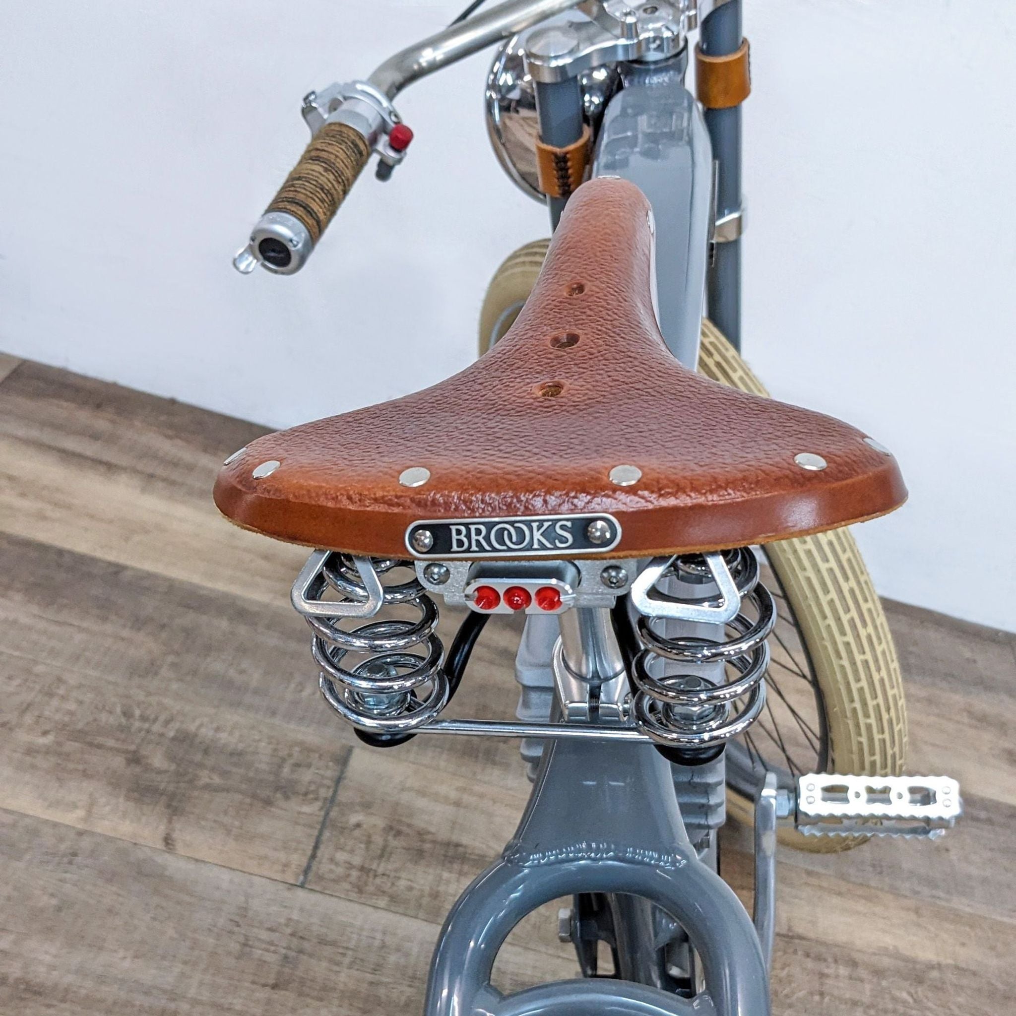 3. Close-up of a brown leather Brooks saddle on a Vintage Electric bicycle, showing the springs and rear red taillights.