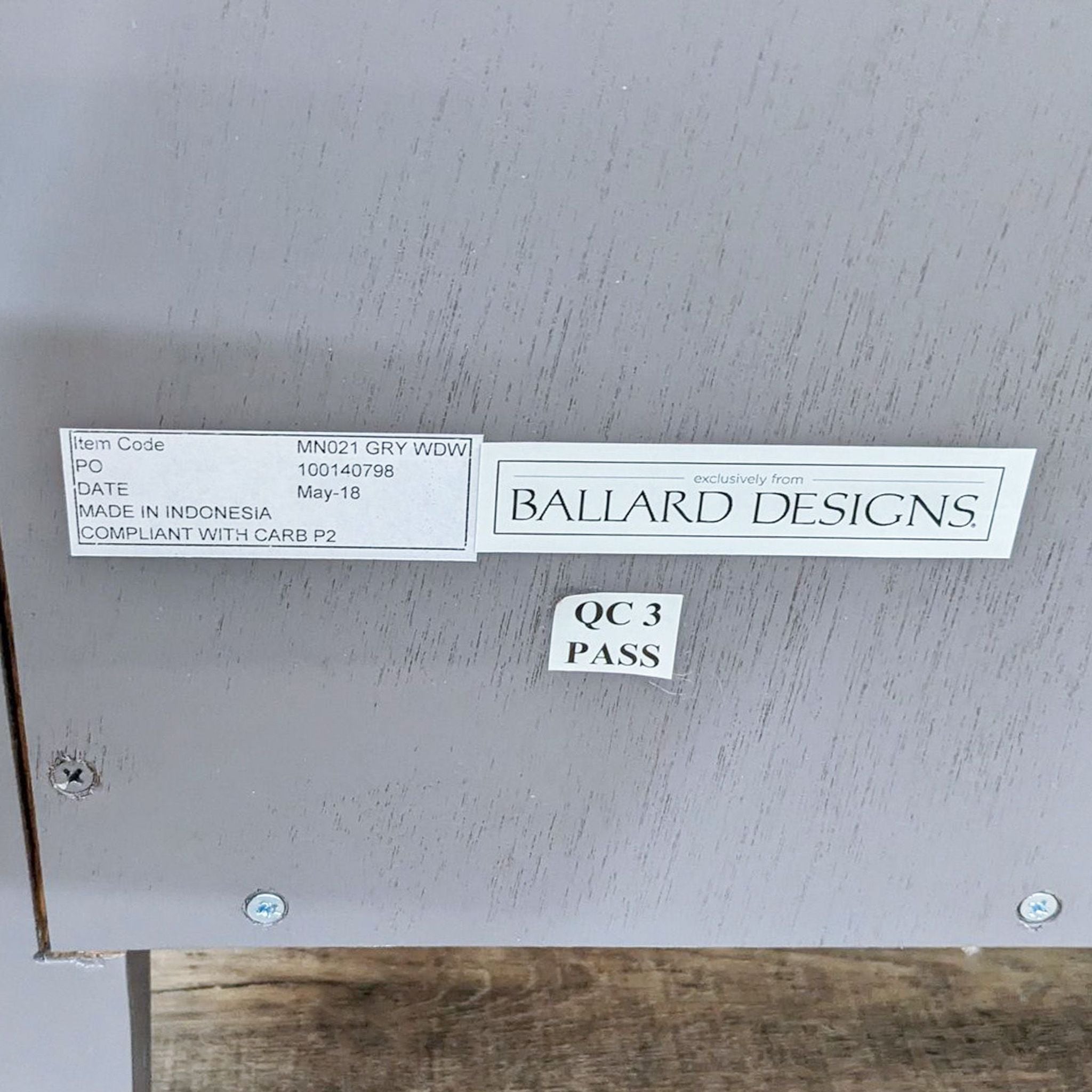 Alt text: Close-up of a Ballard Designs end table's sandblasted hardwood drawer with an information label indicating item code, production date, and quality control pass.