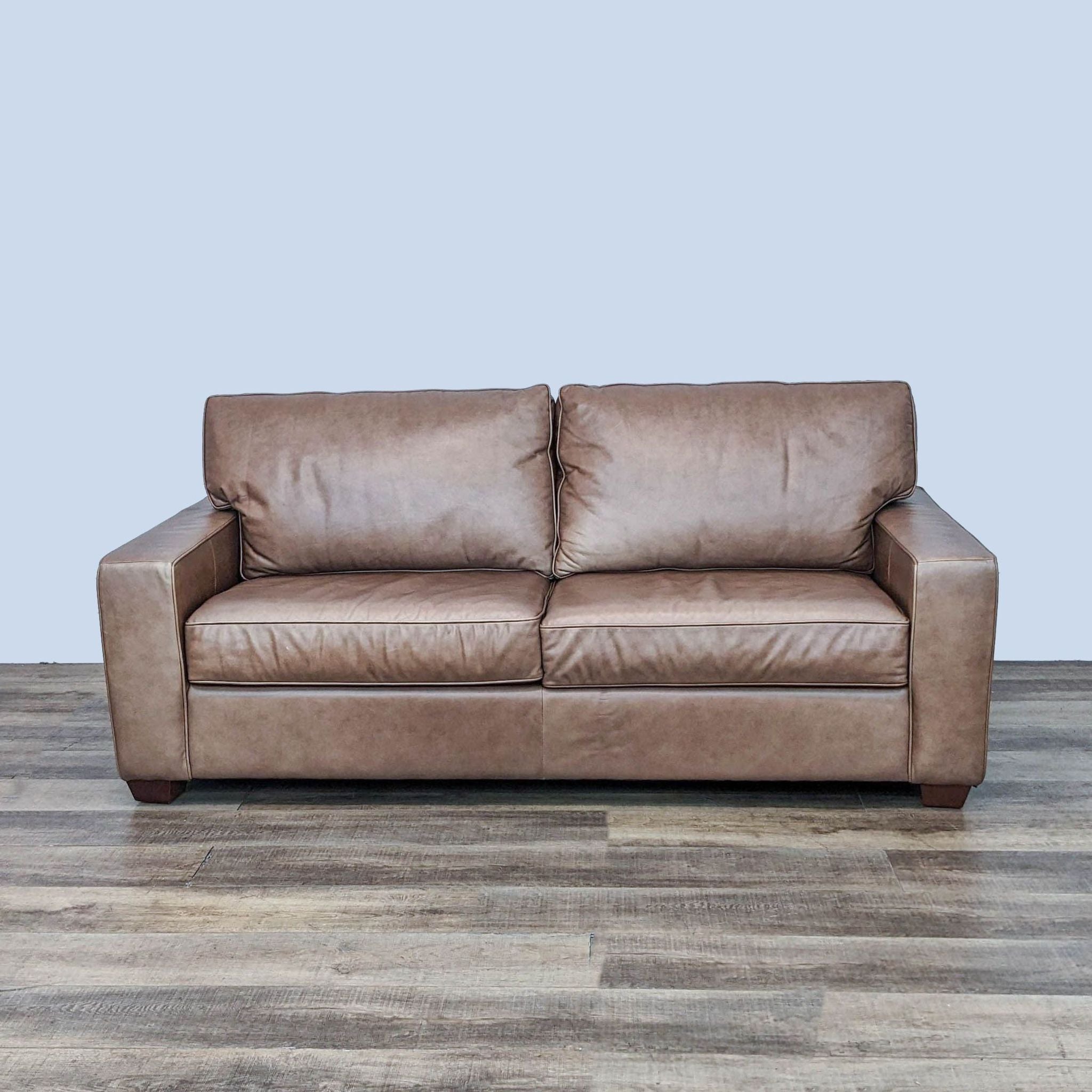 Brown leather two-seater sleeper sofa with track arms and dark wood feet by Pottery Barn in upright position.