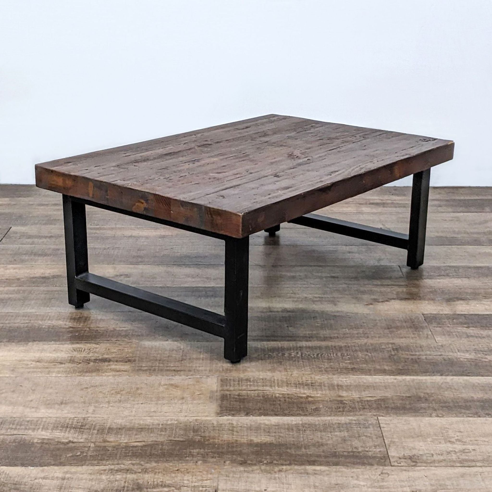 Reclaimed pine wood Reperch coffee table with rustic distressed finish, knots, and black metal legs on a wooden floor.