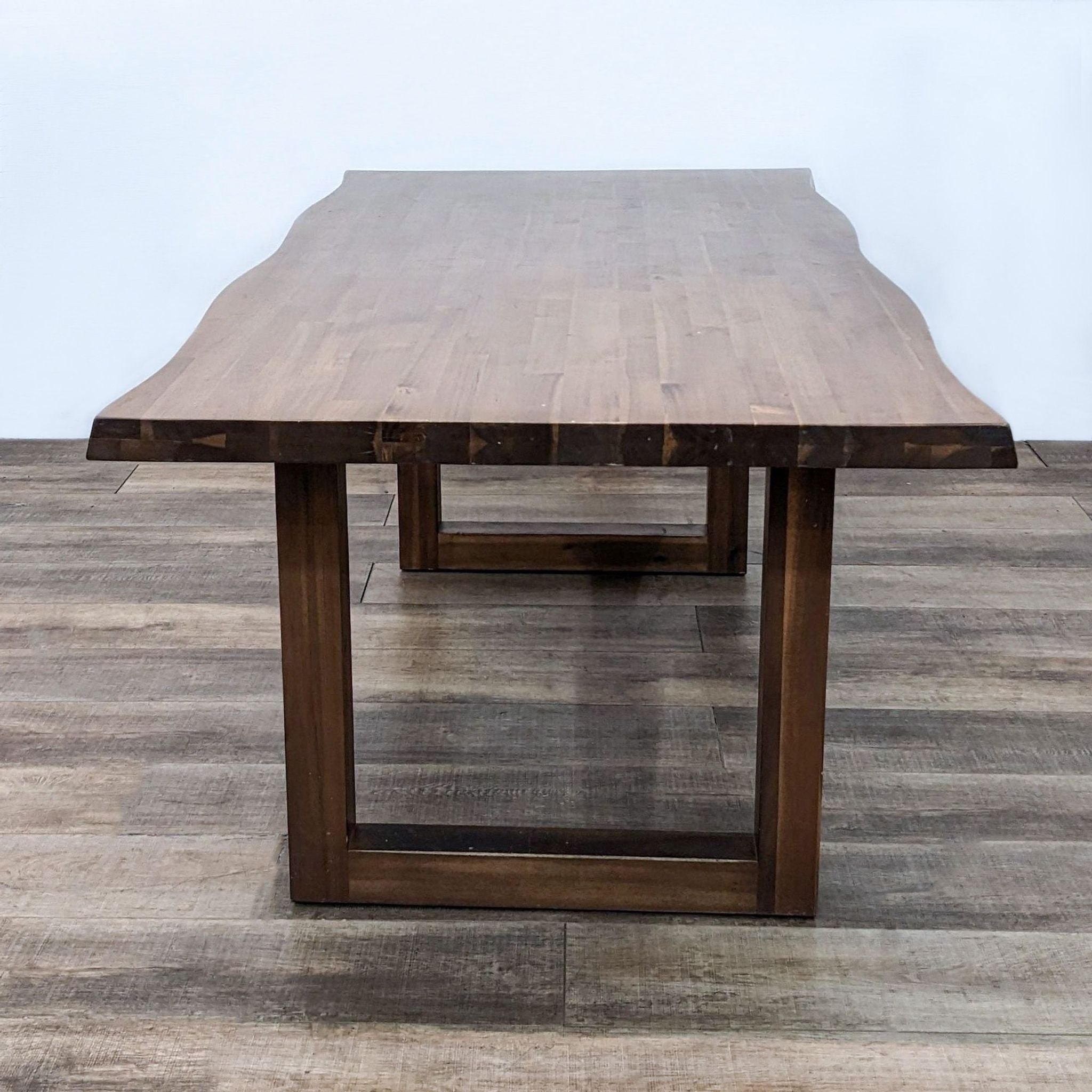 Reperch brand dining table with a live edge wood top and wooden sled base on a herringbone floor.