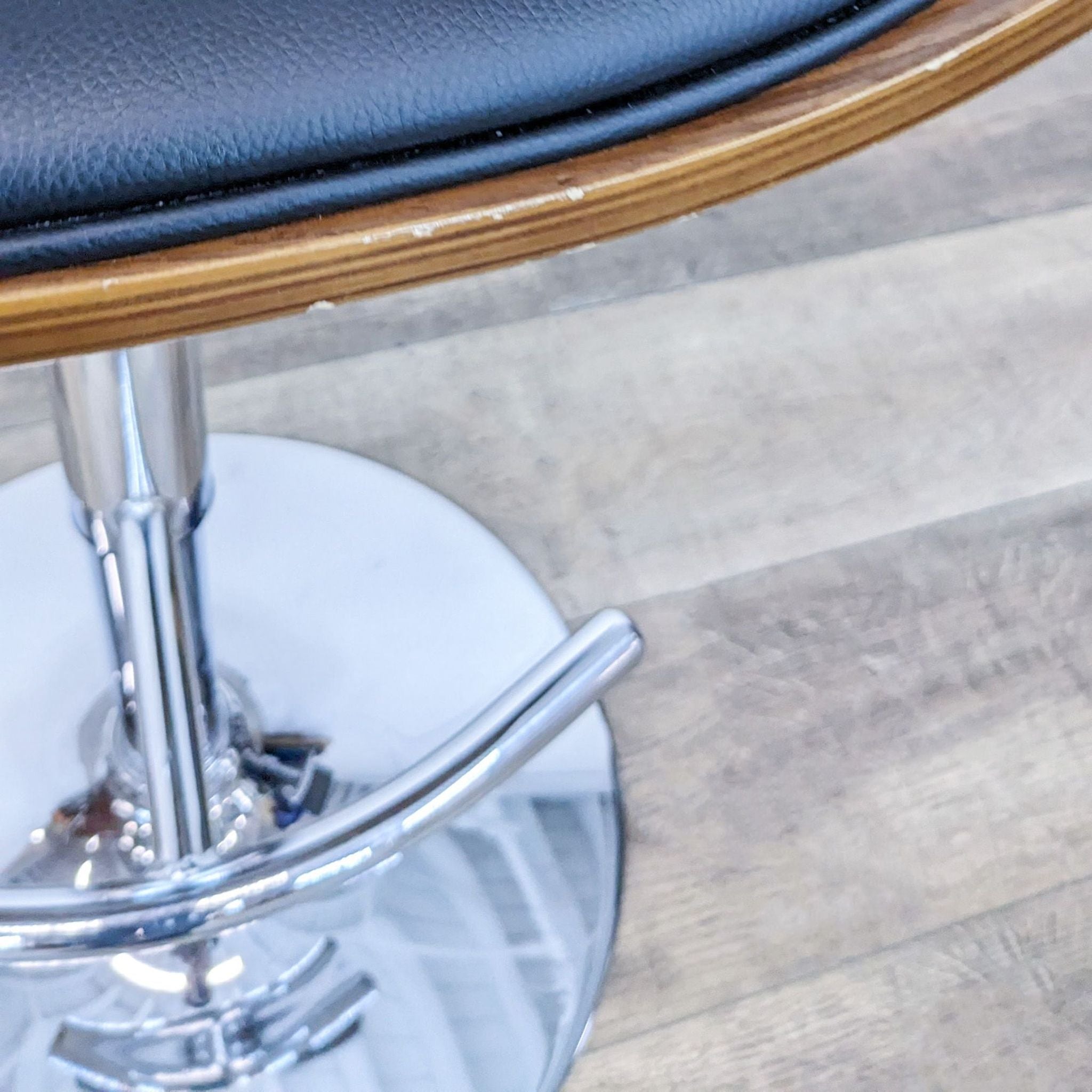 Close-up view of Reperch swivel stool detailing the black padded seat and wood finish.