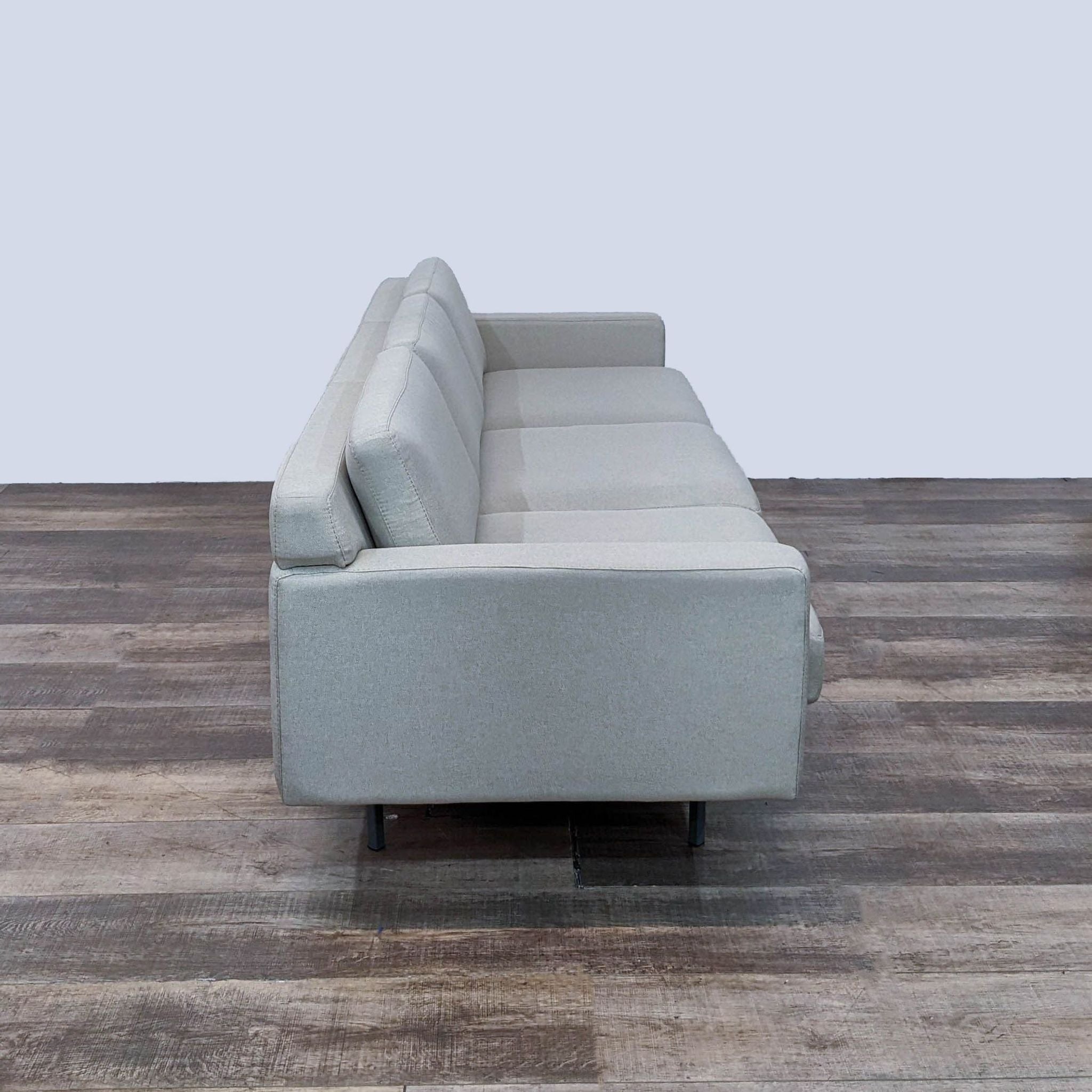 Alt text: 3-seat minimalistic light grey sofa by Rowe Furniture with square arms and black metal feet on a wooden floor.