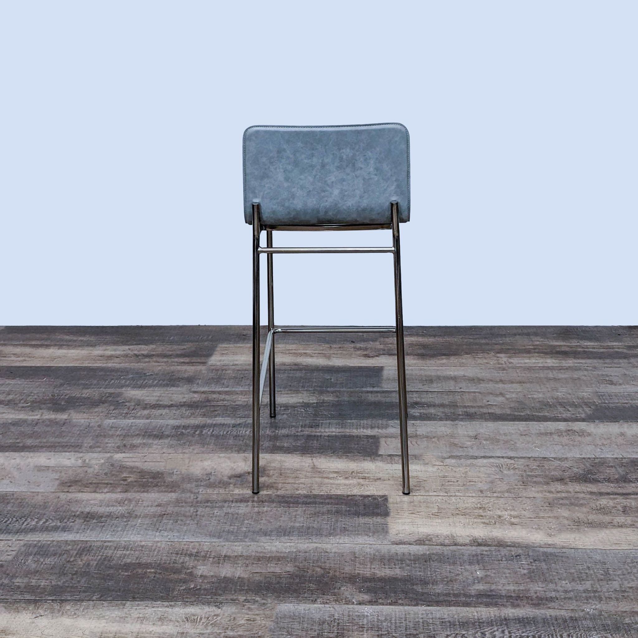 Side view of a contemporary CB2 gray leather Strut barstool featuring a shiny chrome frame on wooden flooring.