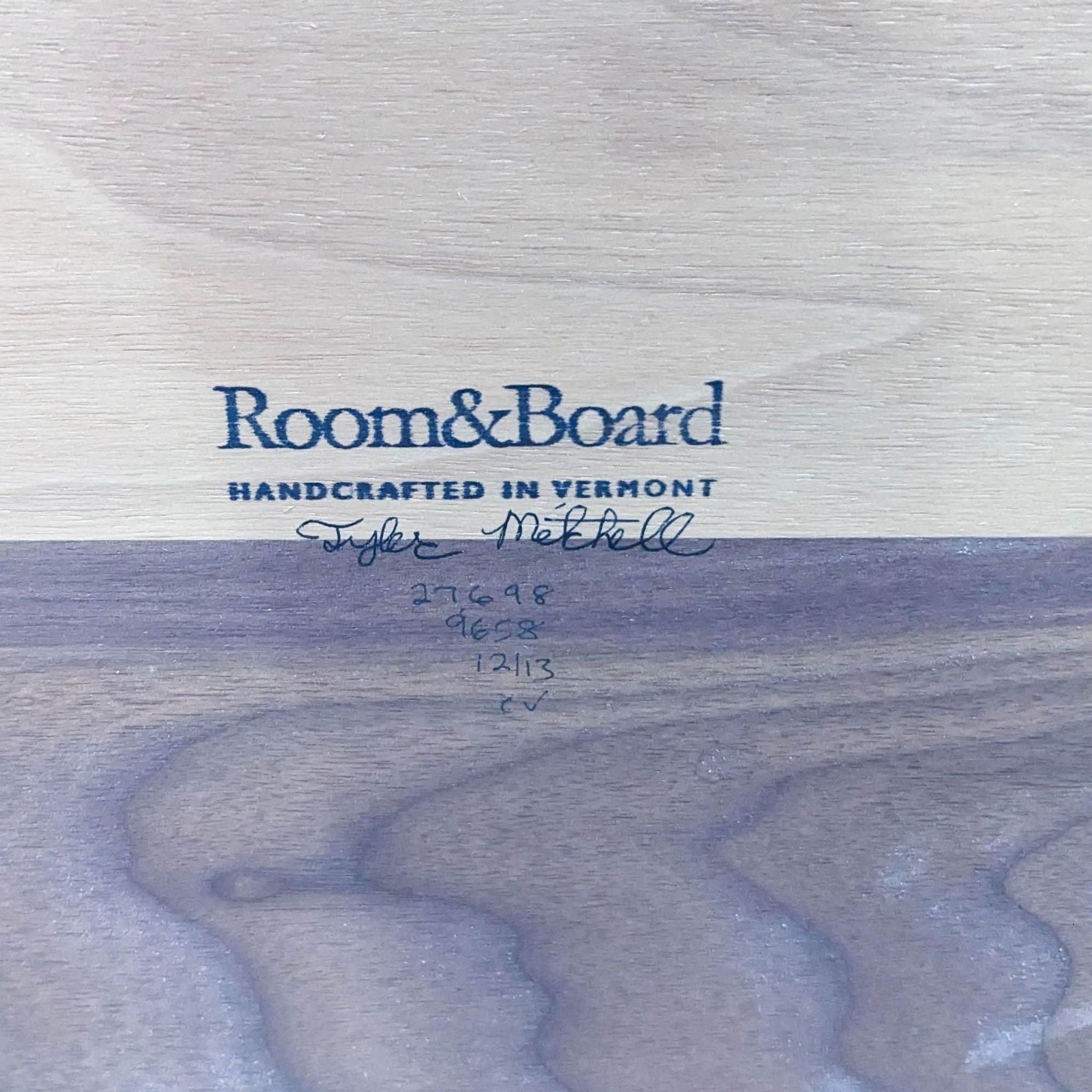 Close-up of Room & Board label on a solid walnut top of a Parsons dining table, with handcrafted in Vermont text and signature.